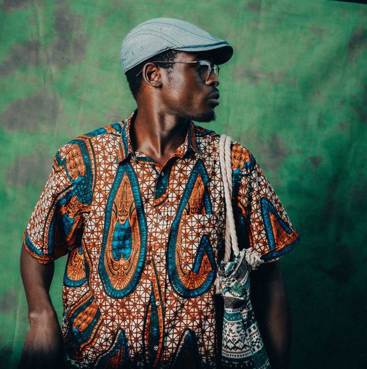 Homme portant une chemise à motifs africains et un sac en tissu en bandoulière, sur fond vert