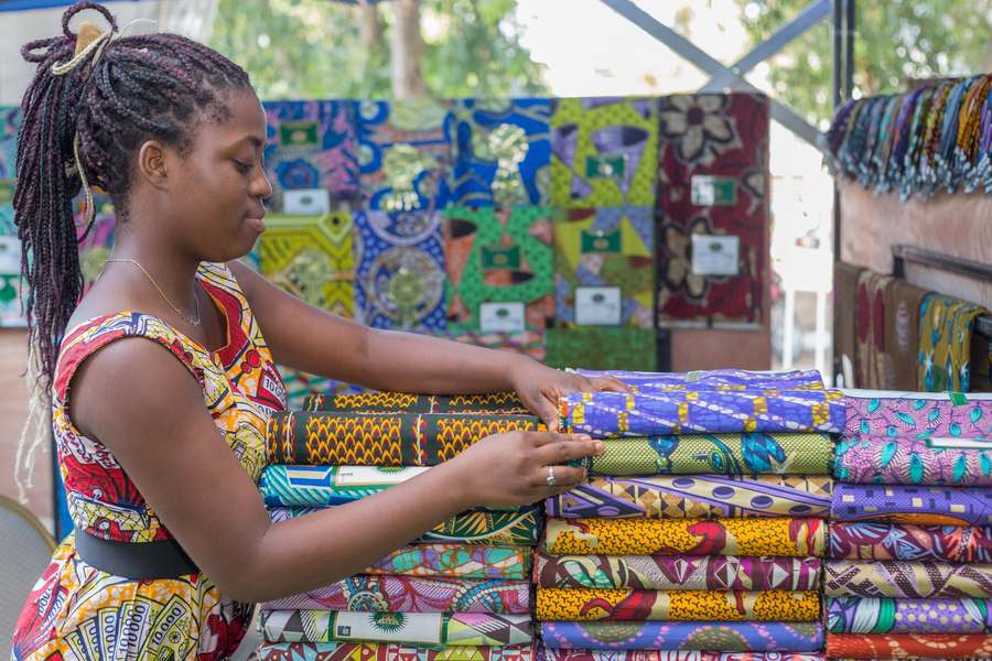 Jeune femme rangeant des piles de pagnes wax colorés sur un étal de marché à Cotonou