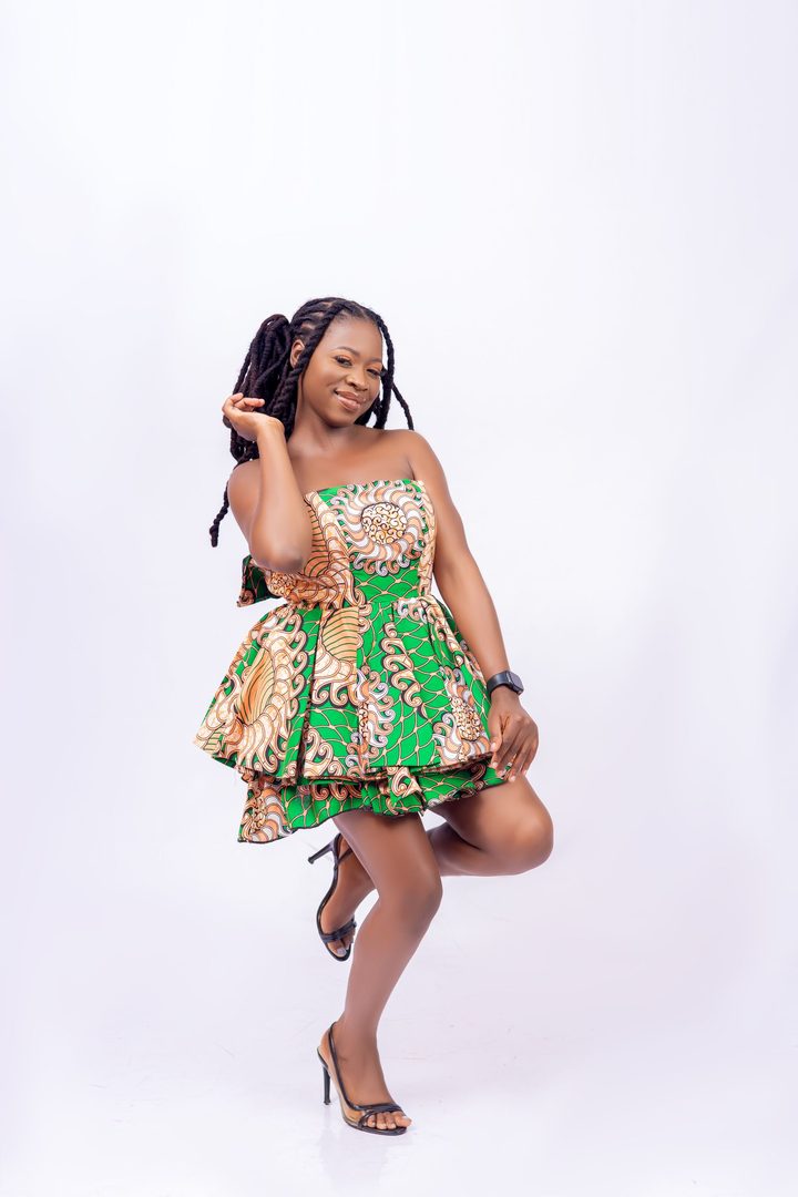 Femme posant sur fond blanc dans une robe courte bustier en wax vert et orange