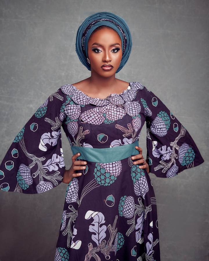 Femme en robe évasée en wax violet à grandes manches, ceinture verte et foulard assorti