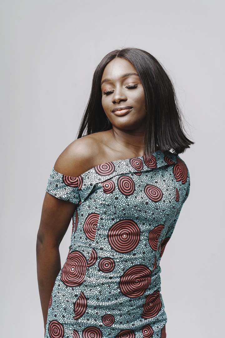 Femme en robe midi ajustée à épaule dénudée, imprimé wax gris et rouge, sur fond gris clair