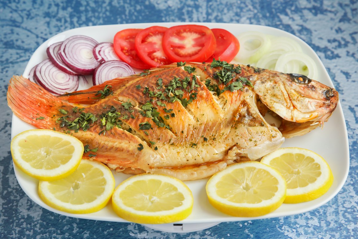 Poisson entier grillé servi avec oignons, tomates et rondelles de citron